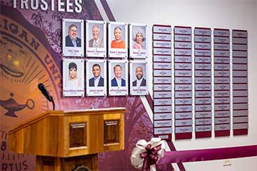 A wooden podium stands in front of a maroon wall covered in photos and metal name plates