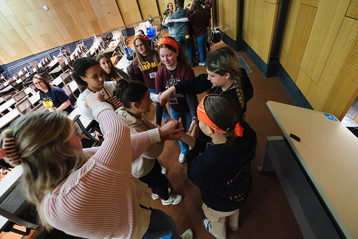 A group of high school students stand in a group at the back of an auditorium.