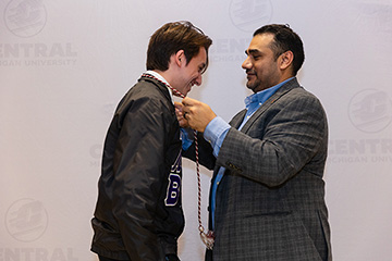 A faculty member places a commencement cord around a student's neck