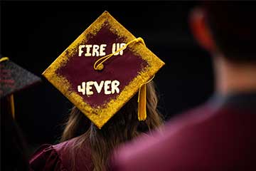 The words Fire Up Forever written in gold glitter adorn a maroon graduation cap during a CMU commencement ceremony