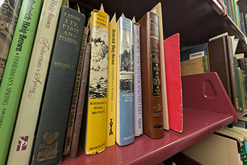 A row of multi-colored books sit on a red metal shelf.