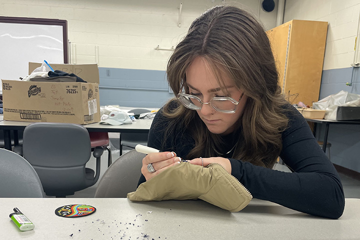 A young woman wearing glasses peers down at a piece of fabric she is working on.