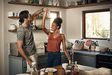 A happy man and woman couple hold hands overhead in a kitchen.