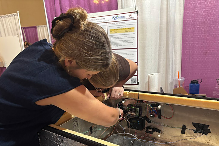 A young woman wearing a blue top and with her hair pulled back into a bun installed electronic circuits while wearing dark nitrile gloves