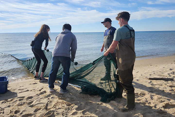 Several young people pull a fishing net from a big body of water