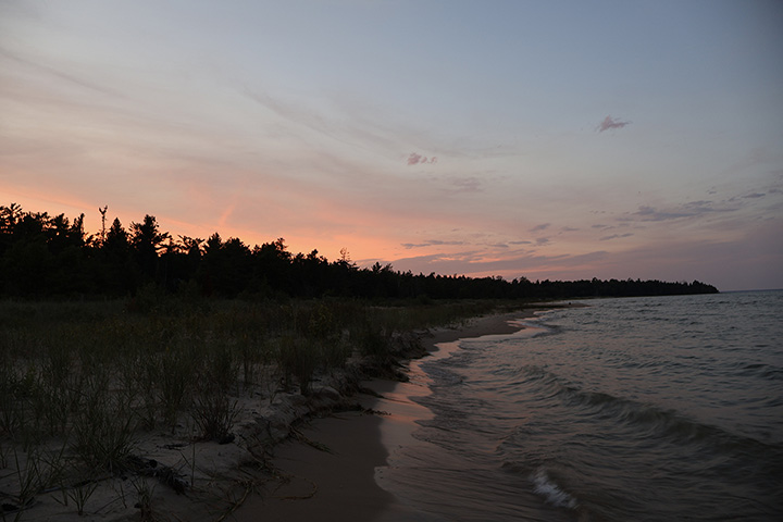 A spit of land stretches out into a lake with the red from the sun visible just over a tree line