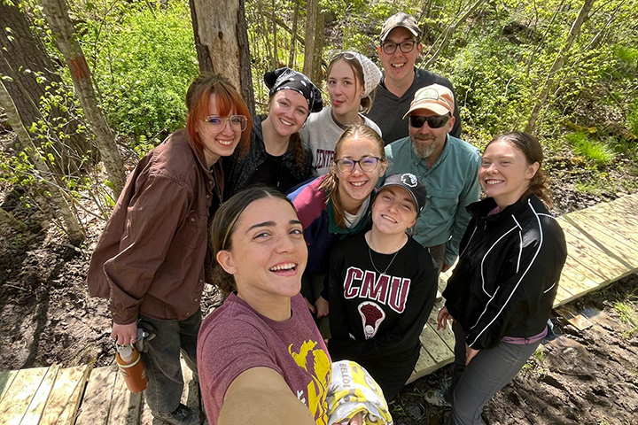 A group of young people pose for a photo on a wooden walkway in the middle of a forest