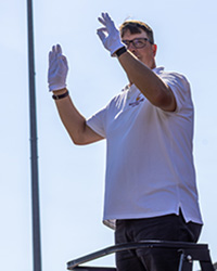 A man in a white shirt and glasses holds two hands in the air