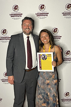 A man in a suit stands next to a young woman in a print dress against a background of a white sheet with leadership institute written on it