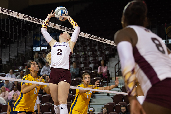 A CMU volleyball player jumps in the air and sets a ball to a teammate