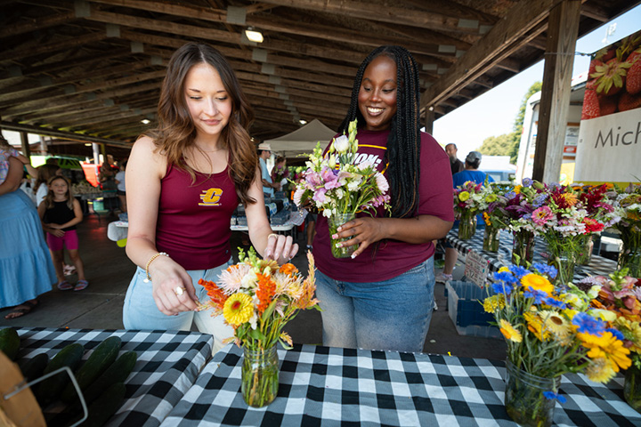 Two college students look at flowers being sold at a farmers market