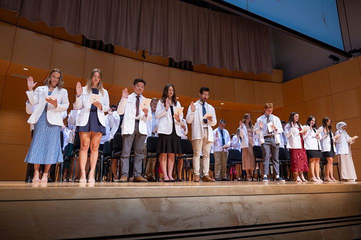 A group of physician assistant students stand on stage receiving their white coats