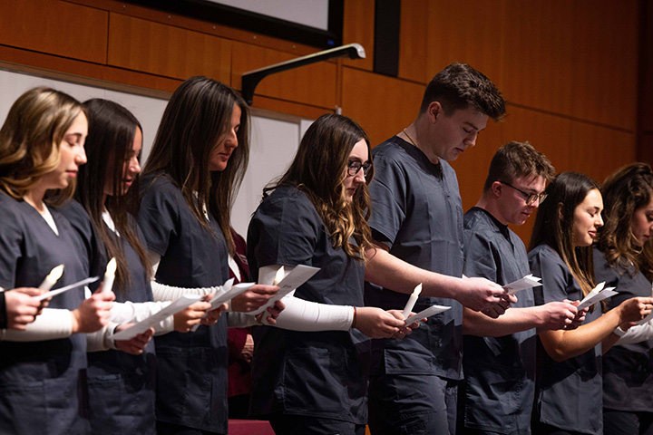 A group of nursing students holding paper and candles while reciting an oath
