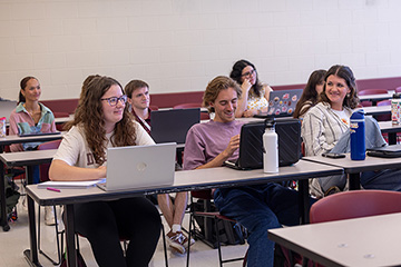 A group of students with laptops sitting at tables in a classroom.
