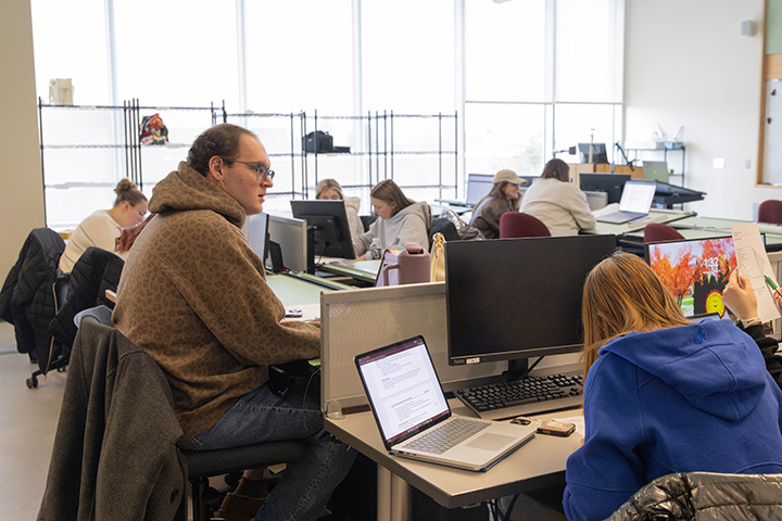 A group of people sitting at desks with computers in a classroom.