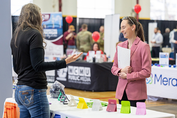 Two people standing around a table at a career fair.