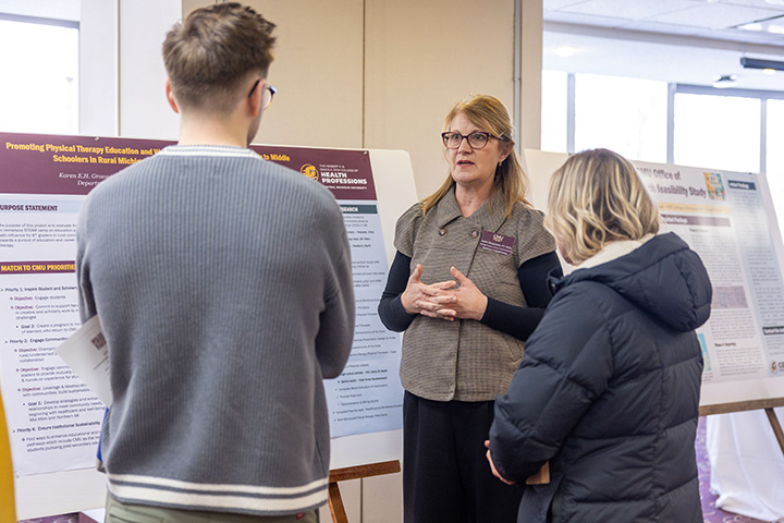 A woman and two other people talk while standing in front of poster boards at a symposium.