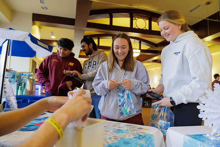 Four CMU students of stand at a table getting free items during the CMU Dining Winter Delightful event