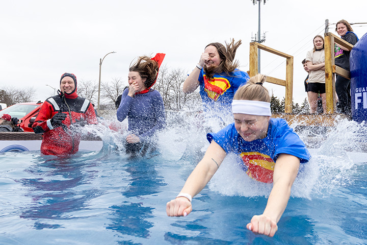 A group group of people in super hero costumes jump into a swimming pool in the winter.