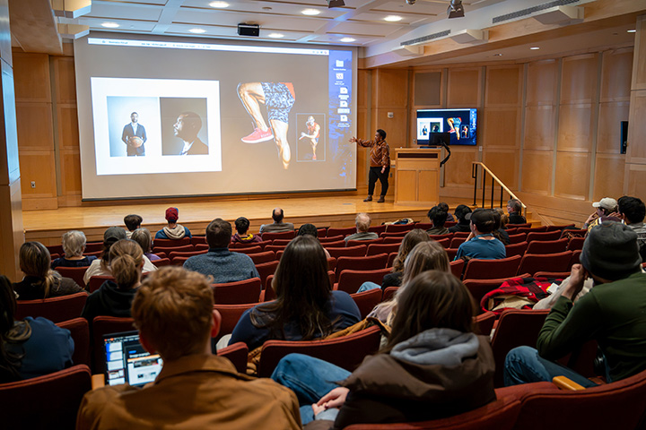 A woman standing on stage in front of a large screen with people sitting in the audience of an auditorium