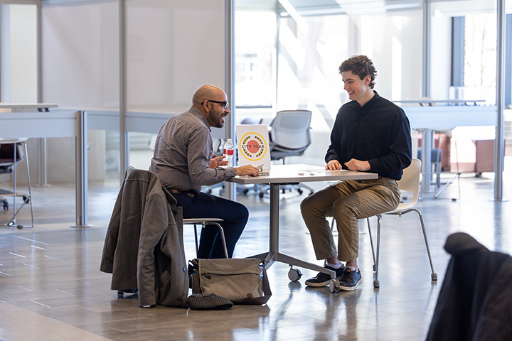 A student and CMU staff member sit at a table having a conversation as part of a mock interview
