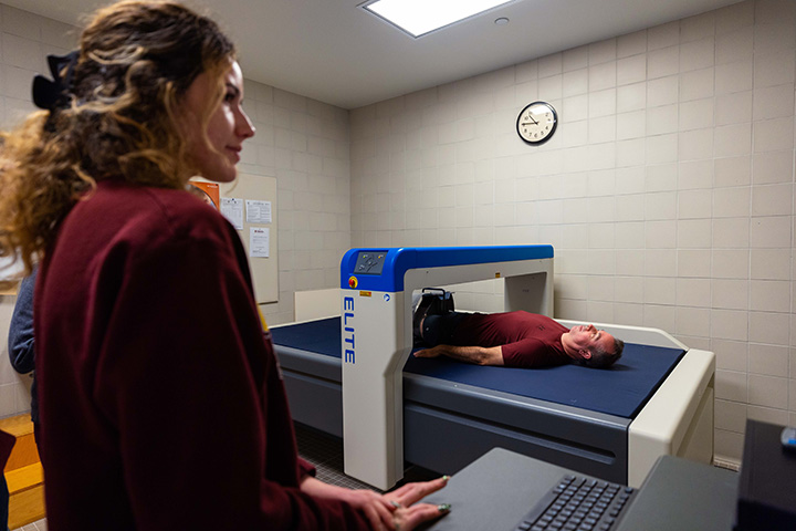CMU President MacKinnon lying in a DEXA scan machine while two people run a computer