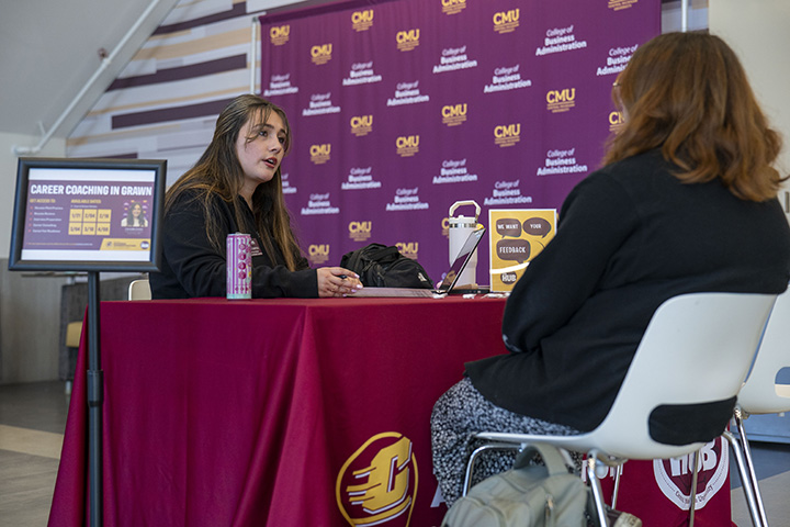 A woman sitting at a table with a maroon tablecloth giving career advice to a student