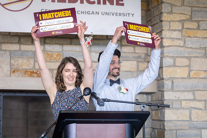 A man and woman medical student each hold I Matched signs at a podium.