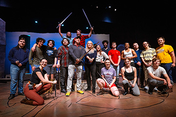 President MacKinnon and theatre students stand for a group photo on a stage.