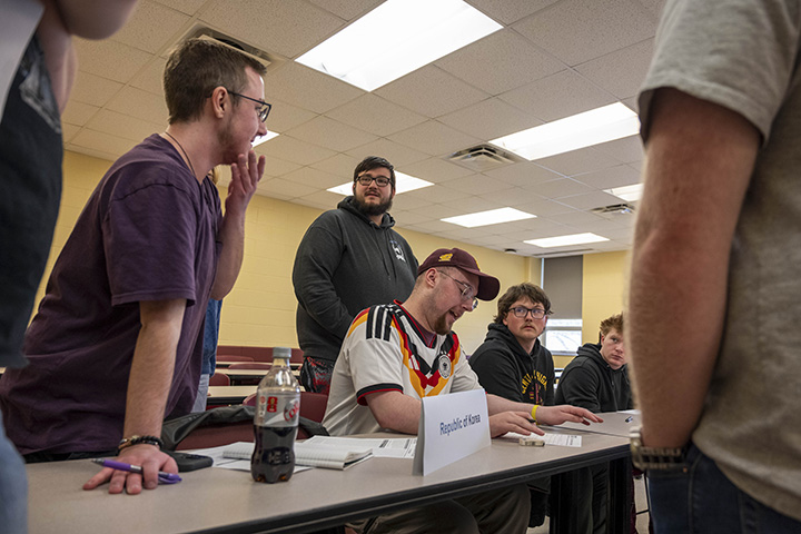 A group of college students stand around a table acting as the Republic of Korea during a Model UN exercise.