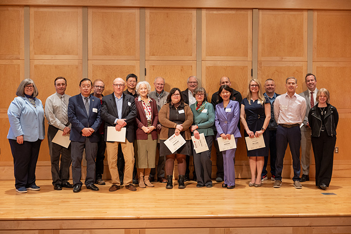 The CMU President and Provost stand with a large group of faculty members on a stage