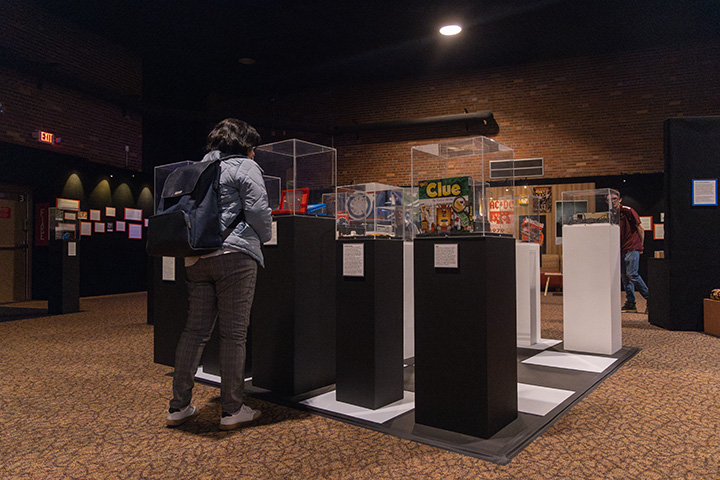 In a large, dimly lit room, people look at vintage board games on display inside glass cases.