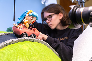 A student works on a stop motion film, adjusting a clay figure in a vehicle.