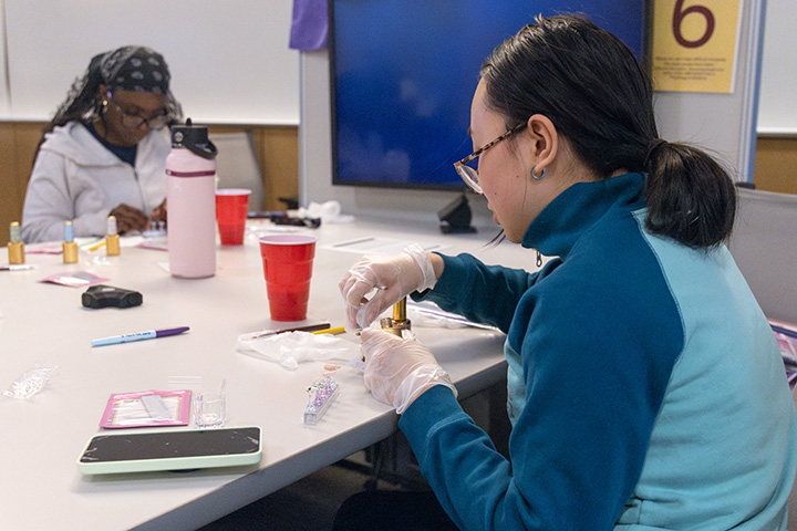 Two students sit at a table doing their nails
