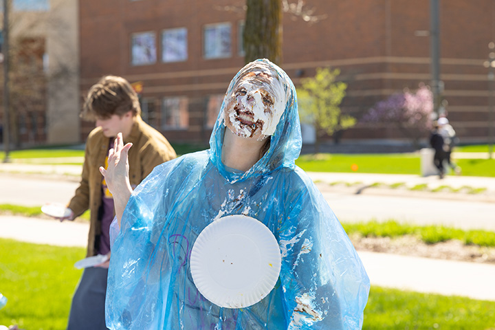 A CMU student wearing a blue poncho smiles after being pied in the face