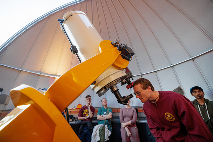 A student looks through a telescope inside the Brooks Astronomical Observatory.