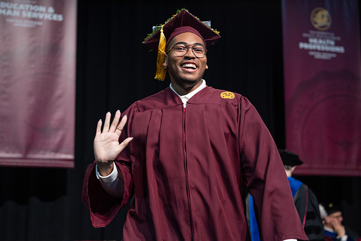 Student Aaron Moore waves and smiles after receiving his diploma