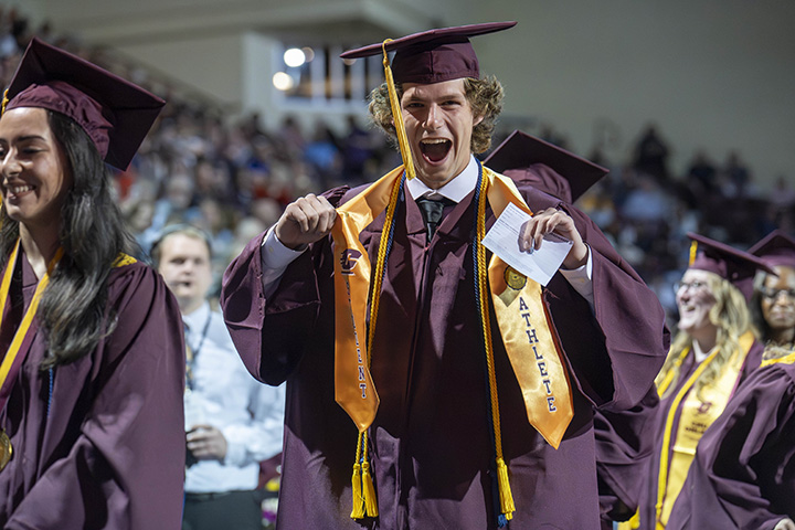 A CMU athlete in graduation attire smiles for the camera on his way to getting his diploma