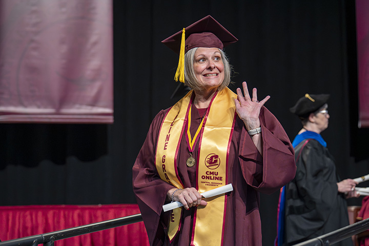 A CMU Online graduate smiles and waves to the crowd while holding her diploma