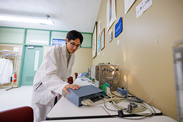 A male student in a lab coat leans over a table touching a computer