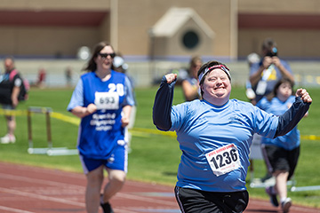 A Special Olympics athlete in a blue shirt smiles while crossing the finish of a track race