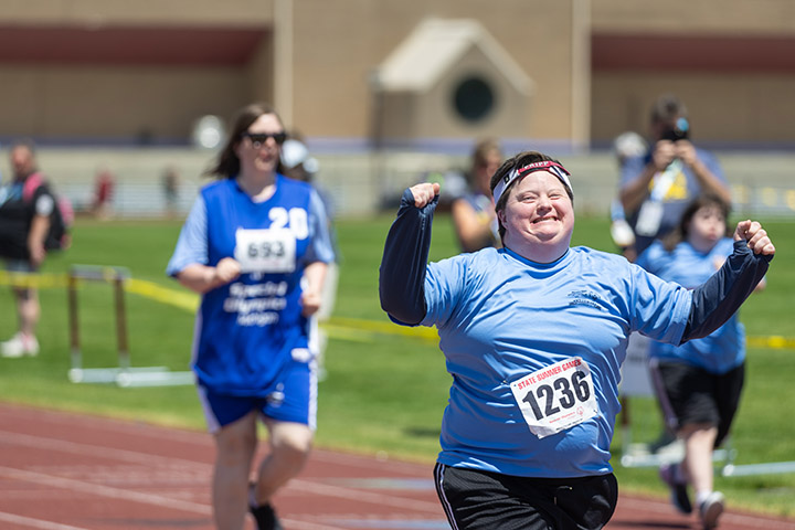 A Special Olympics athlete in a blue shirt smiles while crossing the finish of a track race