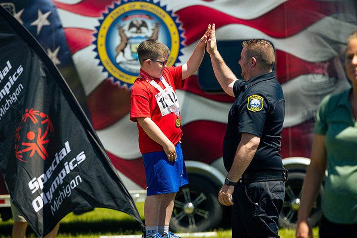 A elementary school-aged Special Olim[ics athlete gives a police officer a high five