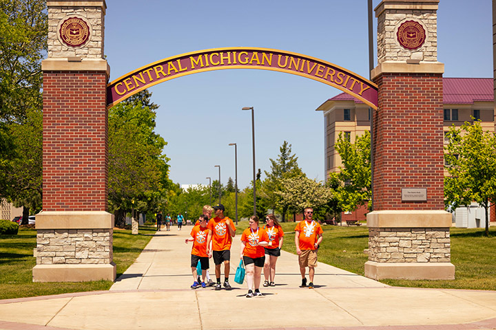 Five people in orange t-shirts walk underneath the CMU Voisin Arch