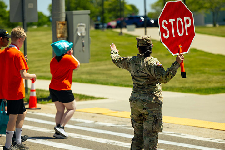 An ROTC member holds a stop sign as pedestrians walk in a crosswalk
