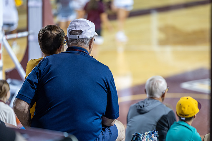 Grand parents and grandchildren sit in the bleachers at McGuirk Arena watching the women's basketball team