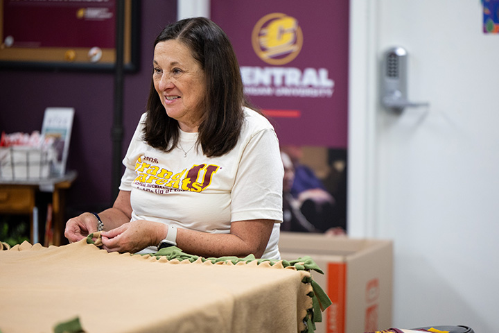 A woman in a Grand Parents U t-shirt sits at a table making a blanket