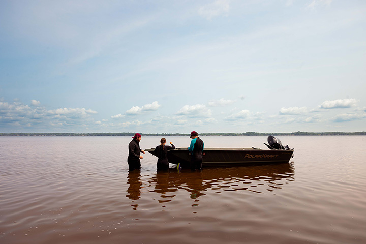 A wide angle shot of a motorboat and three college students in wetsuits