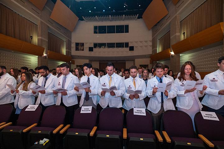 Medical students stand in an auditorium speaking in unison