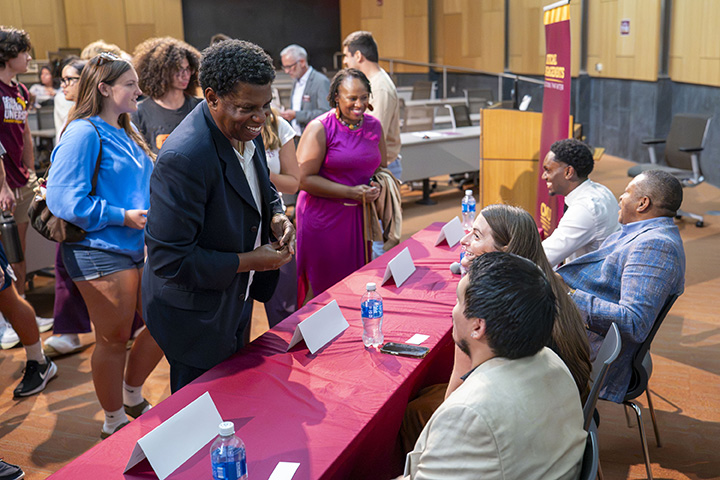 A person walks up to four people at a table during an alumni event called This is My City.